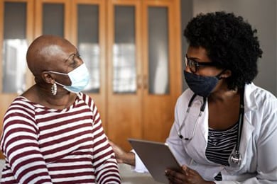 médica y paciente de raza negra de establecimiento de cuidados a largo plazo con mascarilla