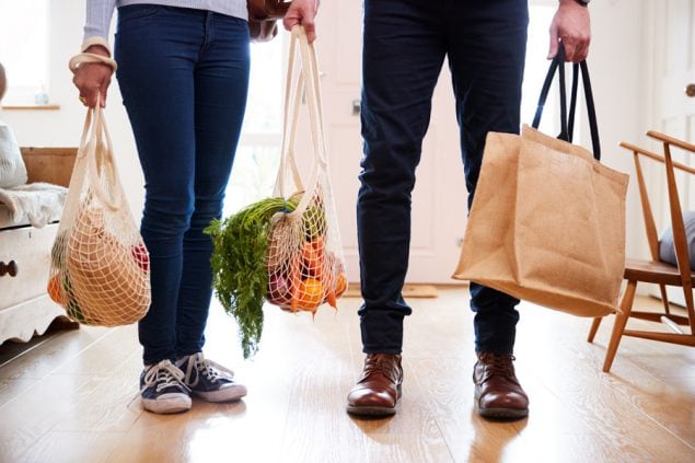 Primer plano de una pareja que regresa a casa tras realizar las compras con bolsas de plástico gratuitas cargadas de comestibles