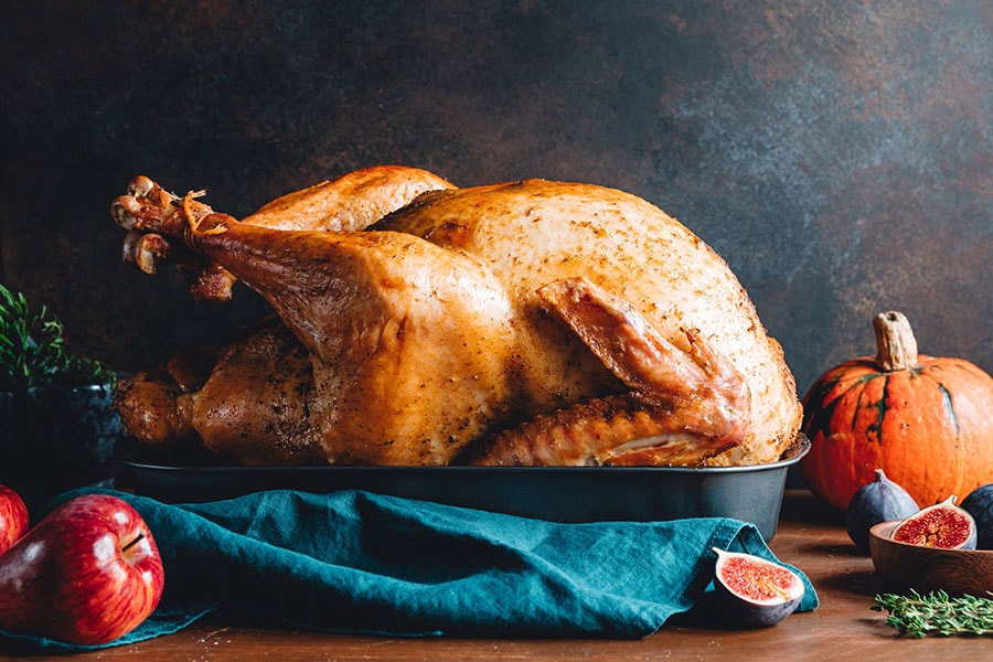 Roasted whole turkey on a table with apple, pumpkin and figs.
