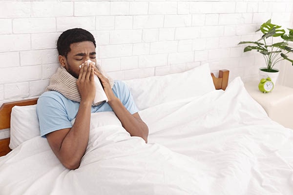 Young sick man in bed cleaning snotty nose