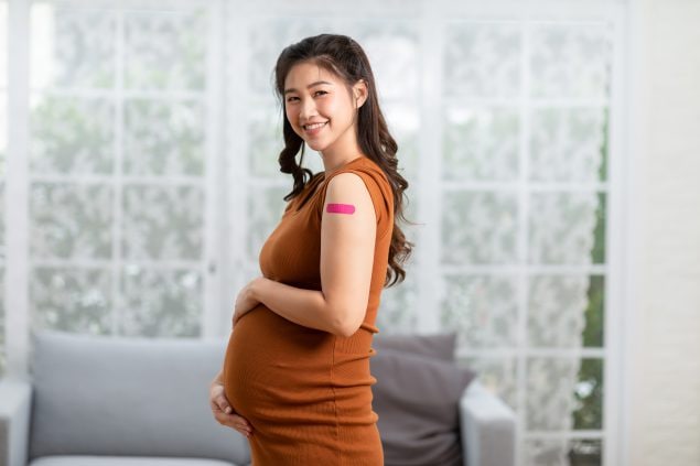 Pregnant person with pink bandage on left arm.
