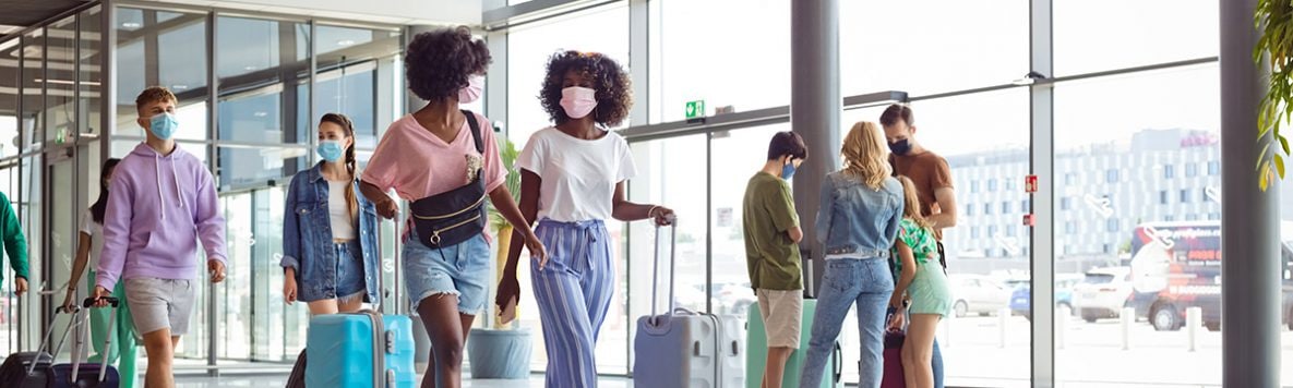 Pasajeros en el aeropuerto con mascarillas N95 llevando equipaje