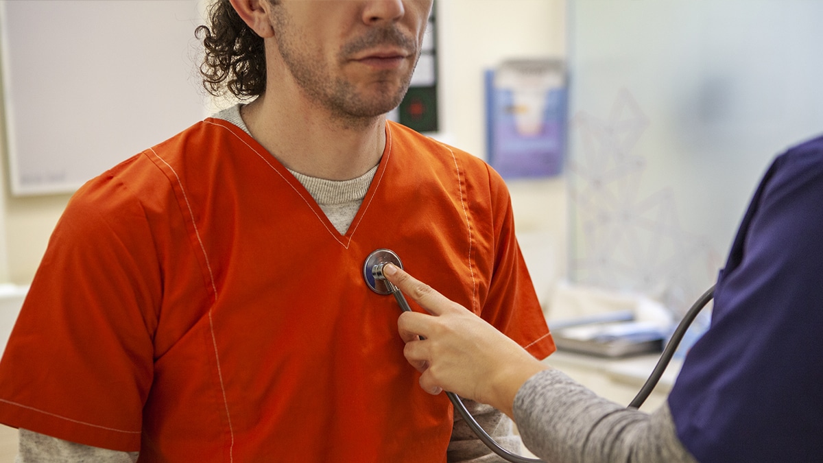 A close-up photo of a physician checking the pulse of a person wearing an orange shirt.