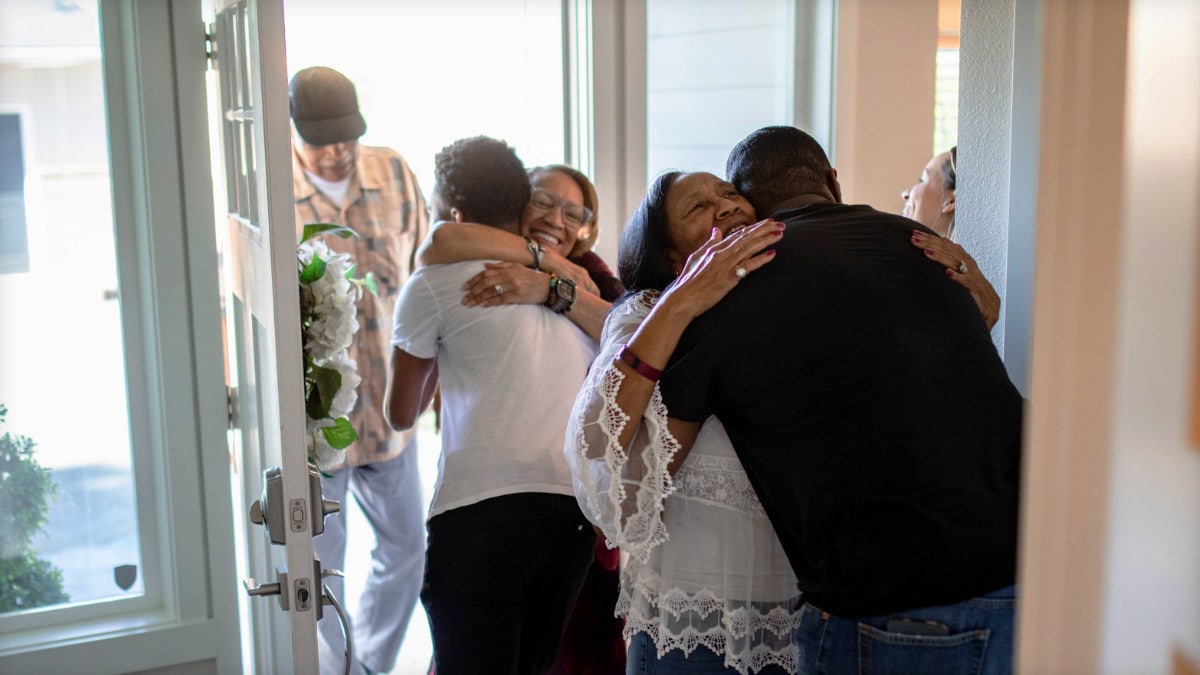 An extended family smile and hug one another as some are coming into the home.