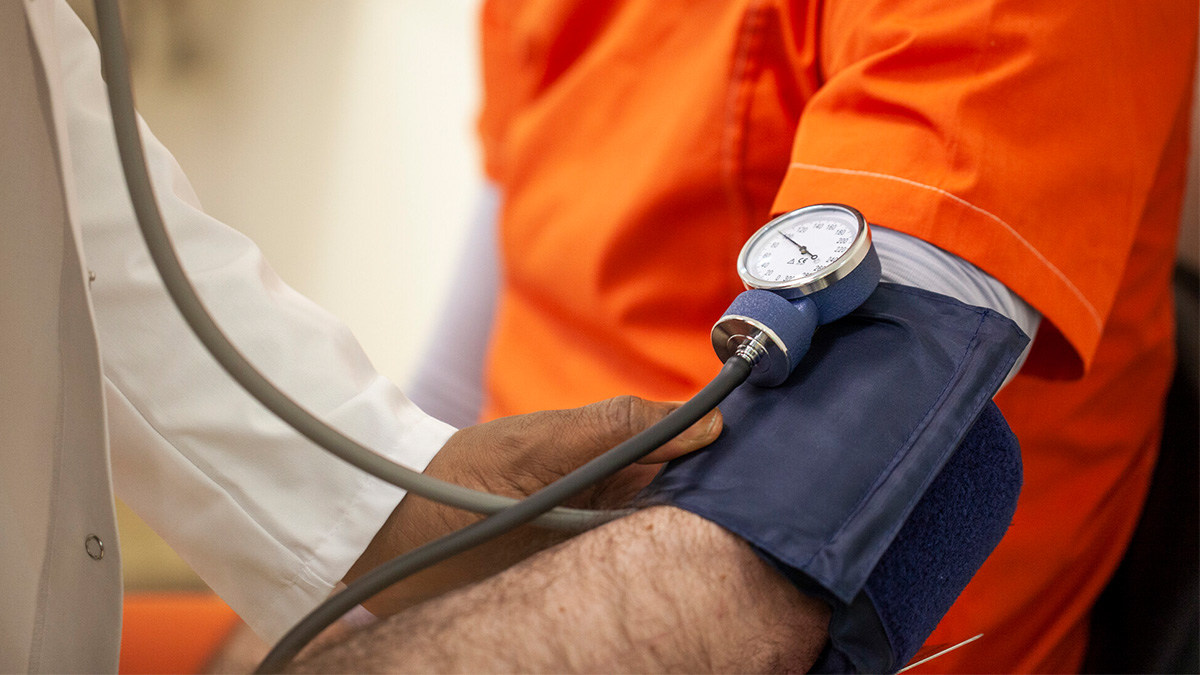 An incarcerated person in an orange jumpsuit receives a blood pressure test from a doctor.