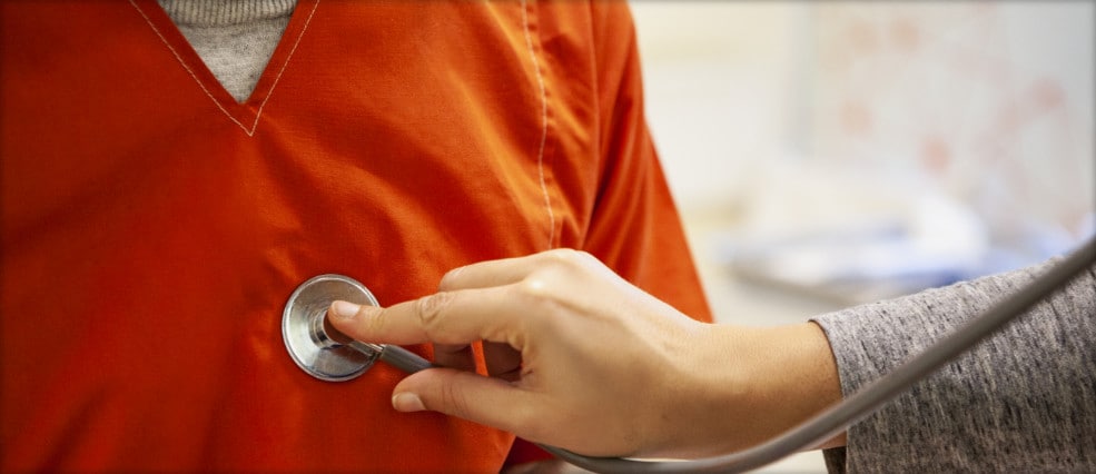 A close-up photo of a physician checking the pulse of a person wearing an orange shirt