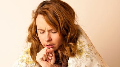 A female young adult sneezing or coughing with a blanket wrapped around her shoulders