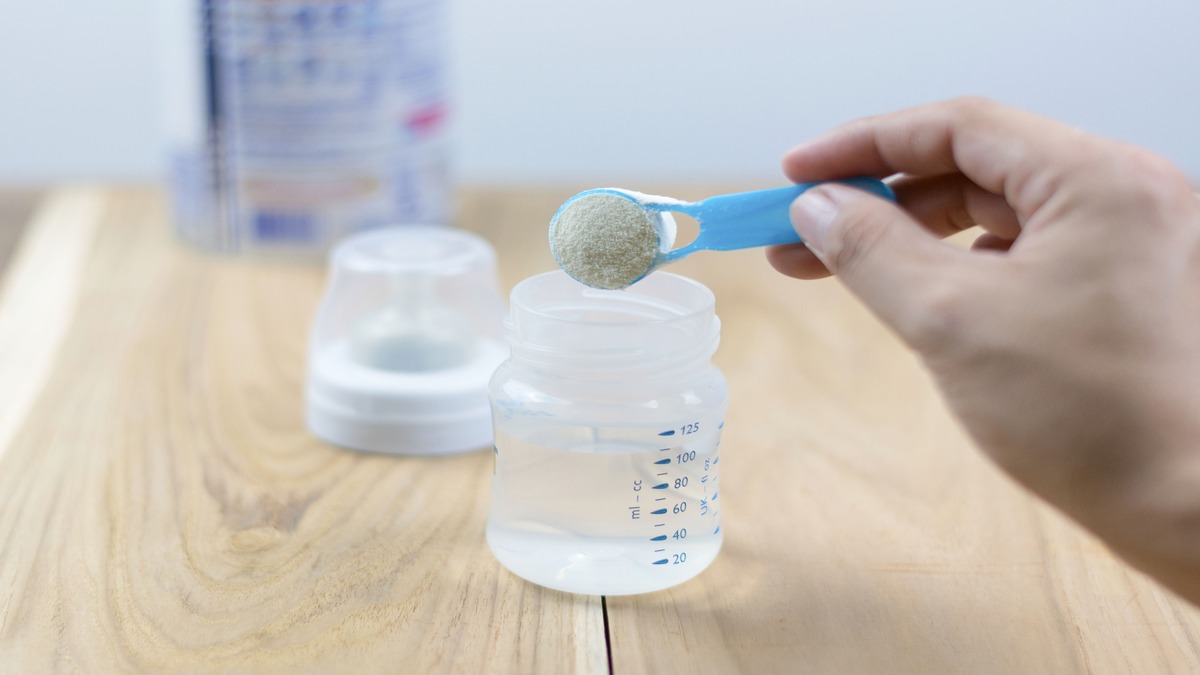 Powdered infant formula in a blue spoon being dumped into baby bottle.