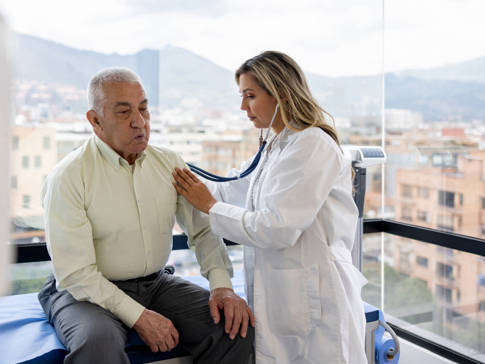 A female healthcare provider using a stethoscope to examine an older man.
