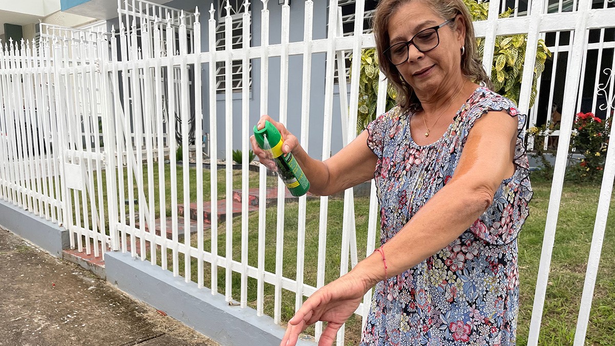 An older woman sprays insect repellent on her arm.