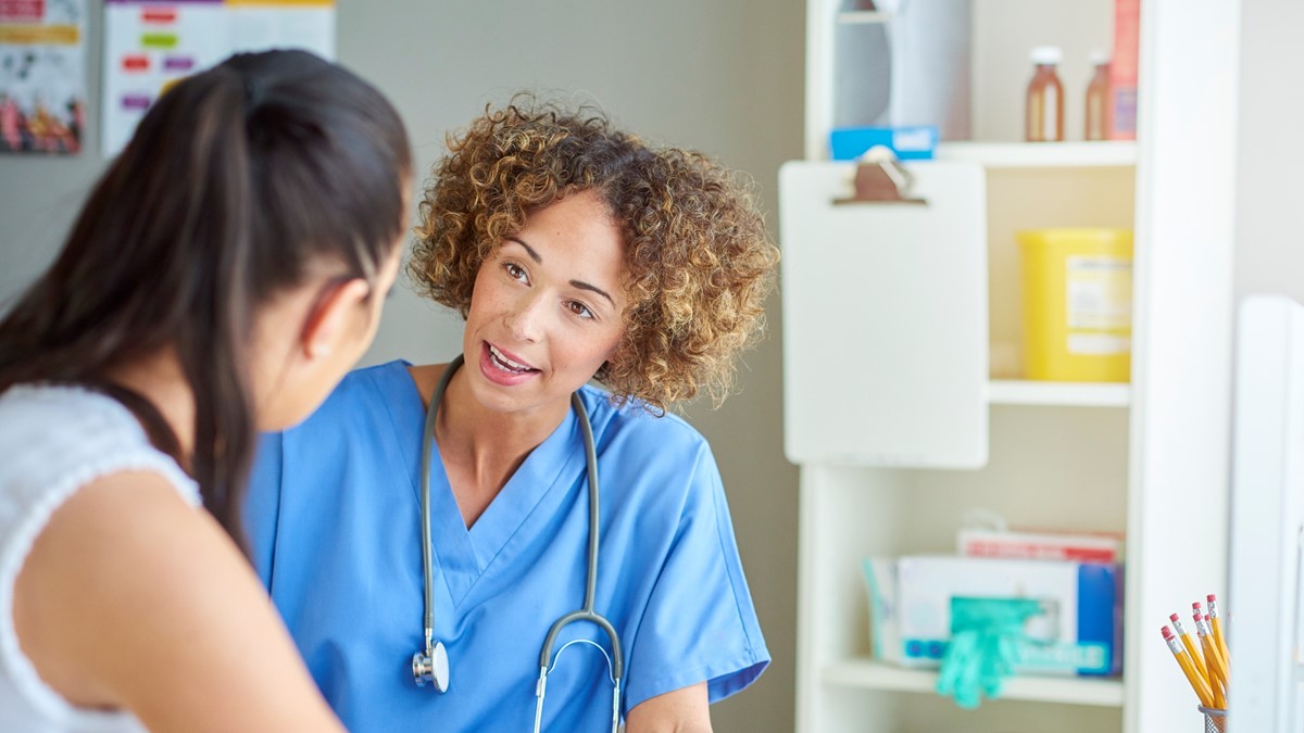 A healthcare provider speaking to a patient in an exam room.