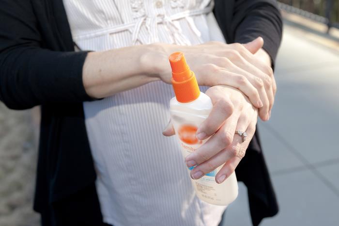 A pregnant person applying insect repellent.