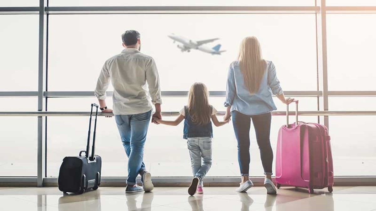 Tres personas con maletas mirando un avión en el cielo.