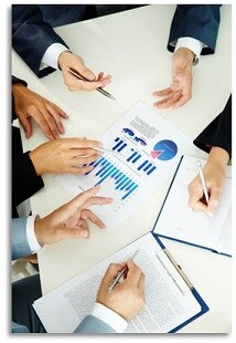 A group of men around a conference table looking at charts.