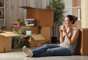 Mujer joven sentada en su apartamento, rodeada de cajas de mudanza