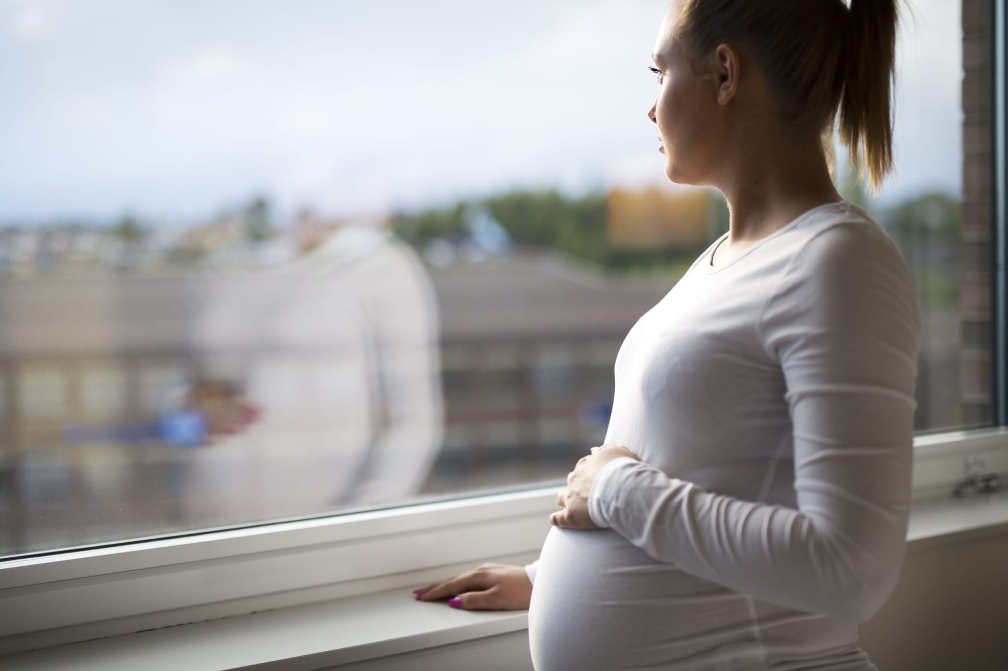 Una mujer embarazada pensativa mirando por la ventana.