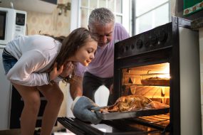 Grandfather and granddaughter check turkey in the oven