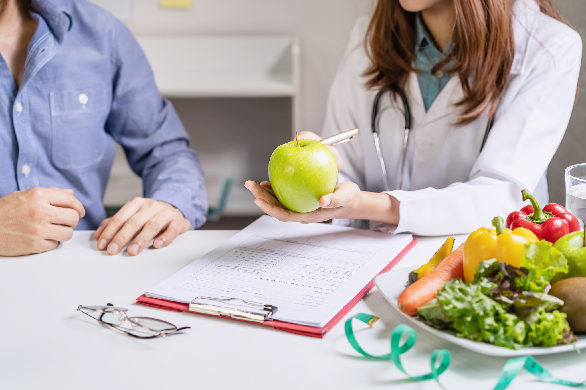 Una dietista o nutricionista atendiendo a un paciente, se ve un plato con una variedad de frutas y vegetales.