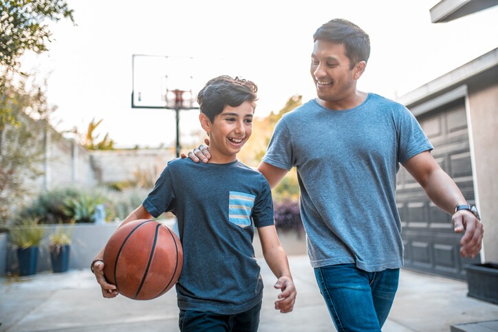 A man and a boy are outside playing basketball.