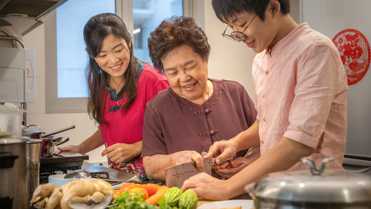 Hombre asiático joven aprendiendo de su madre y abuela a preparar alimentos.