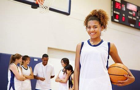 Jovencita atlética sosteniendo una pelota de baloncesto en un gimnasio