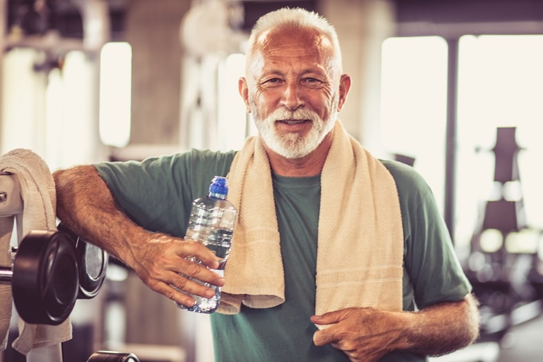 Hombre mayor en el gimnasio sosteniendo una botella de agua