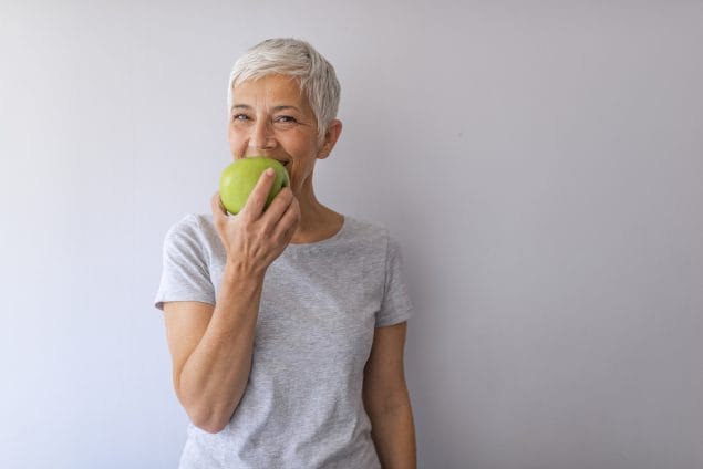 Mature woman with short gray hair eating a green apple.