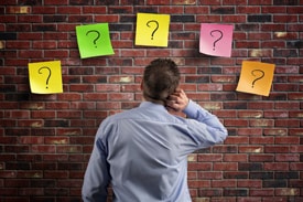 Man staring at brick wall with five question marks on it