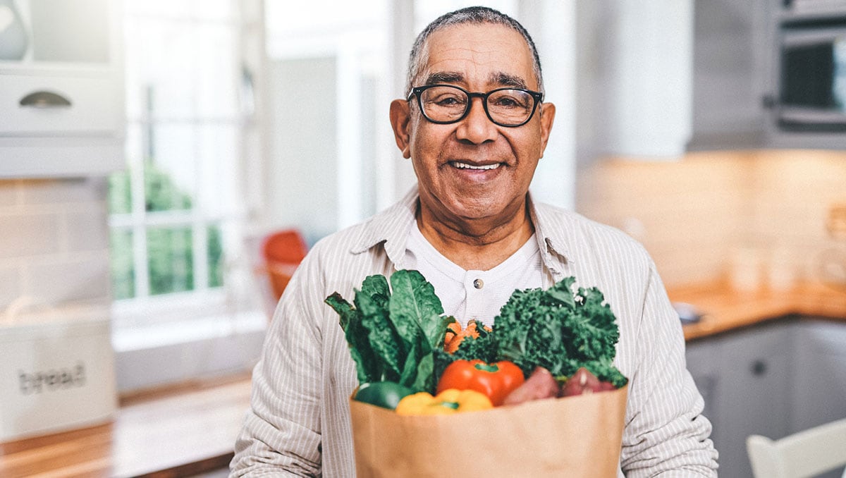 Shot of a elderly man holding a grocery bag in the kitchen