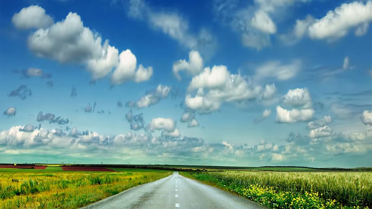 A highway stretching off to the horizon on a sunny day with puffy clouds