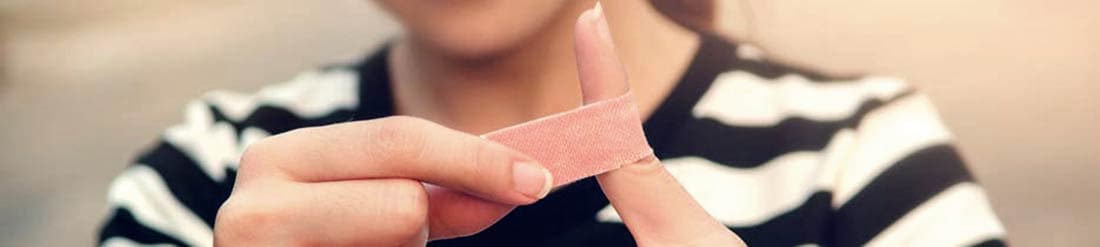 A picture of a young woman putting an adhesive bandage on her finger.