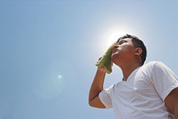 A man in the hot sun wipes the sweat from is forehead with a towel.