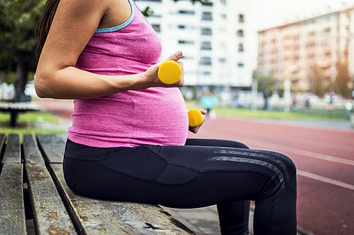 A pregnant women sitting on a bench exercising on a hot day.