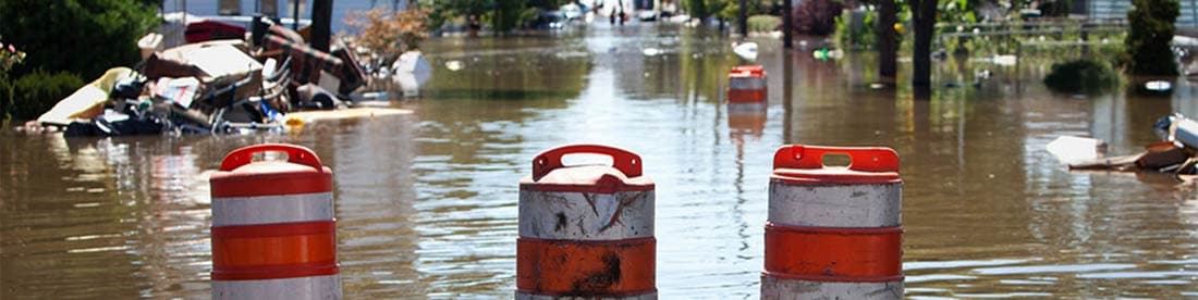 orange blockade barrels float down a flooded city street