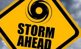 A yellow caution sign on a road that says STORM AHEAD and has an icon of a hurricane.