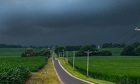 Dark clouds loom over fields and a rural road