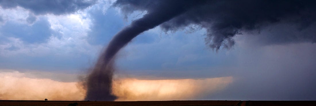 The spout of a large tornado throws debris in the air as it crosses an open field