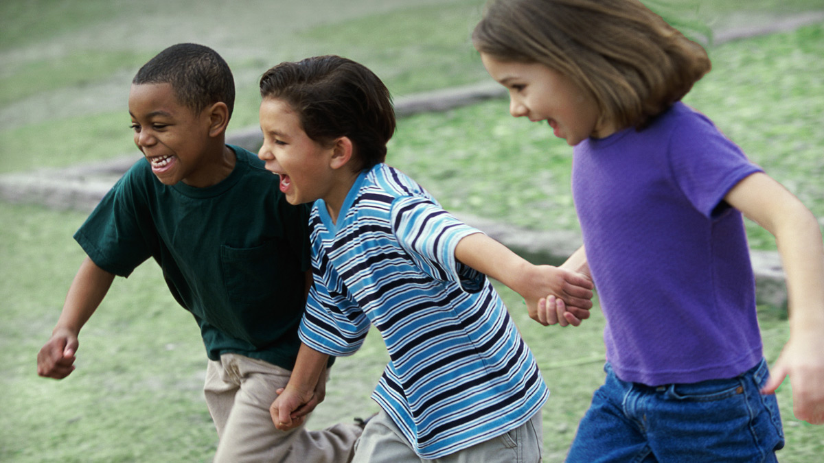 Three children holding hands and running in a field.