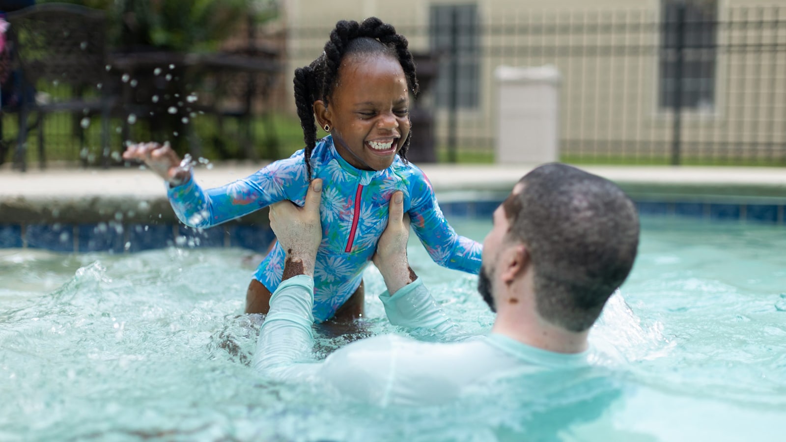 Black father and daughter play in swimming pool.