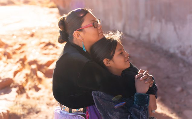 Navajo American Indian sisters hugging under the sunlight of a reservation landscape