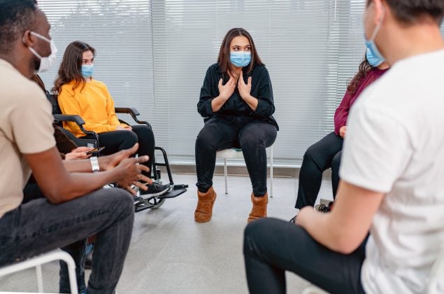Photo of a female doctor wearing a mask talking to a male patient wearing a mask