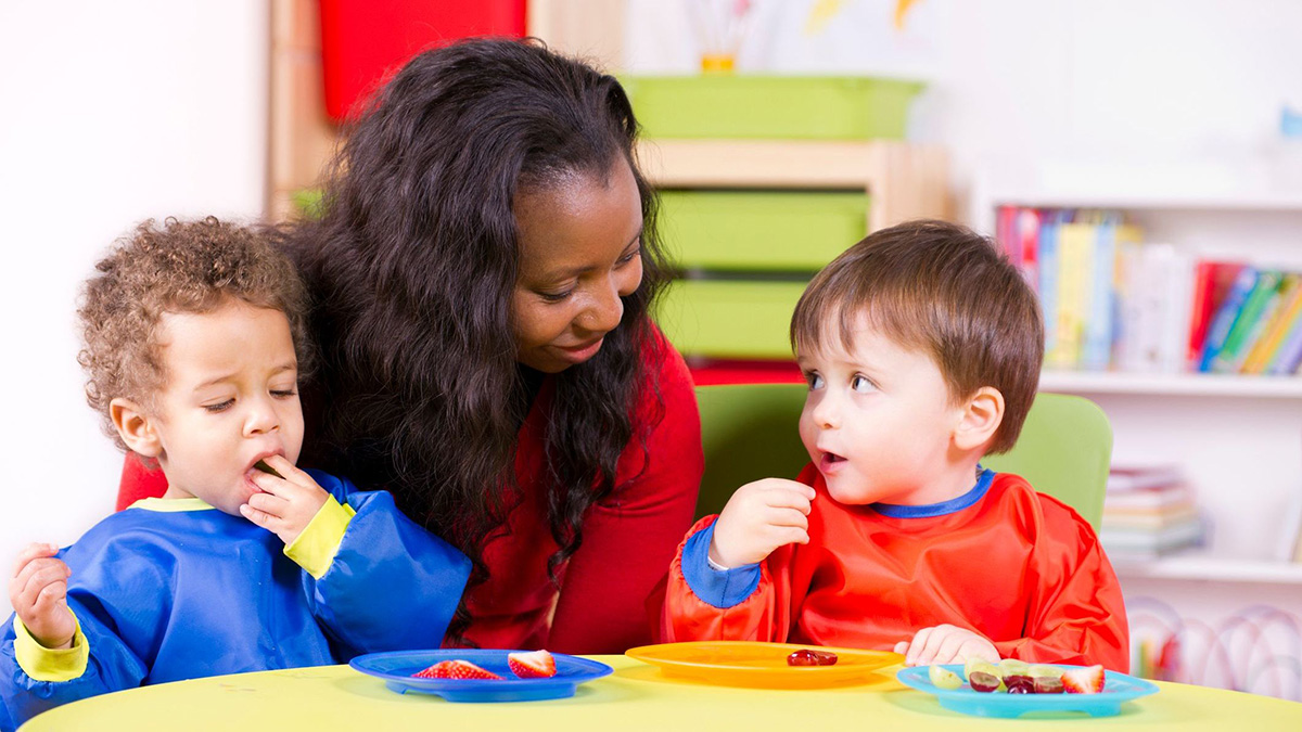 Children eating fruit at a nursery with their care giver