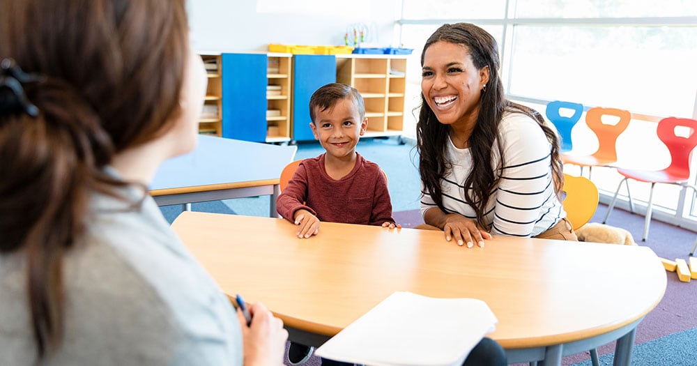 Young boy watches mom and teacher in meeting