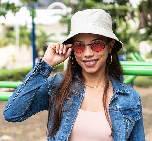 Young woman outdoors wearing hat, sunglasses, and long sleeves