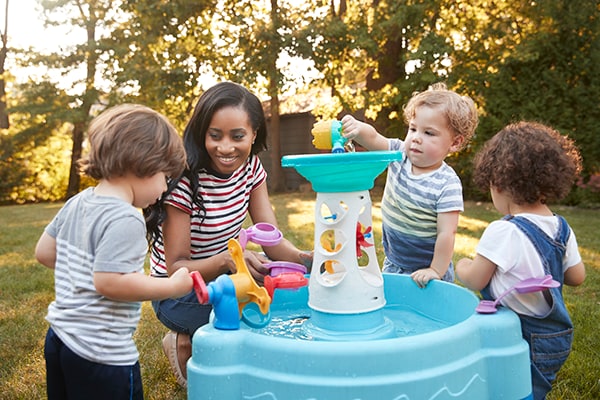 An early care and education provider and young children playing outdoors with water toys