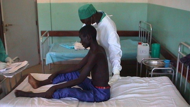 A healthcare provider examines a male Ebola survivor who is sitting on a hospital bed.