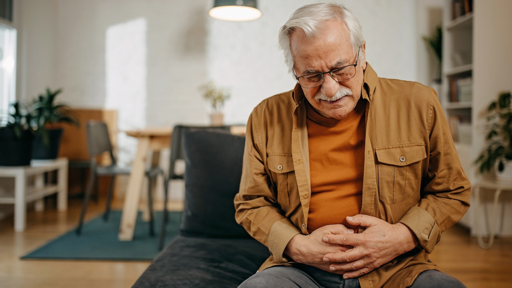 An older adult sitting in a chair holding their stomach in pain.