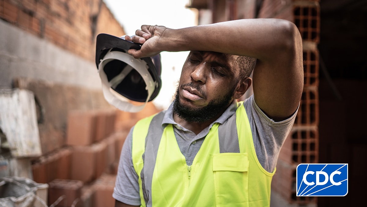 Construction worker wiping the sweat from his brow, standing next to a brick wall