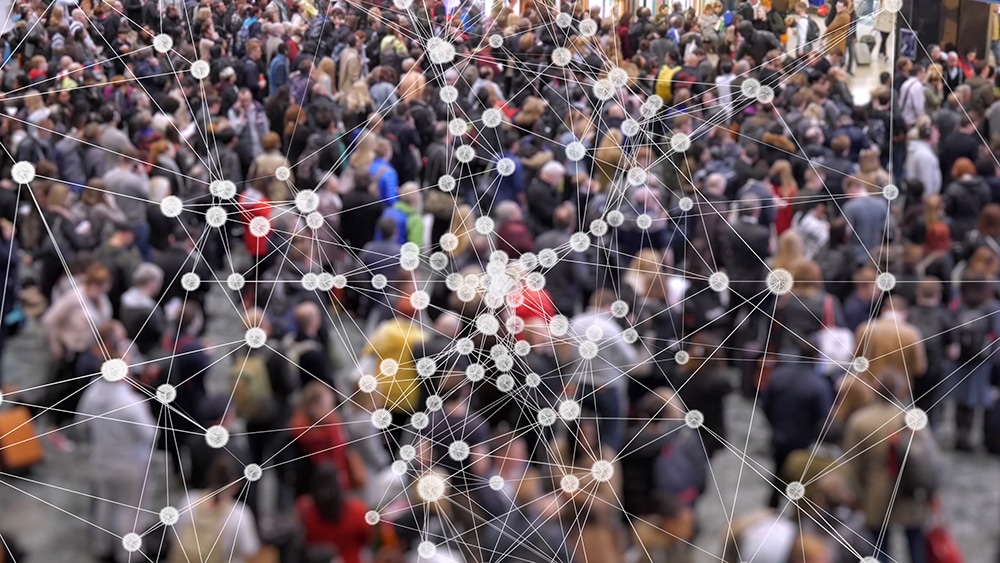 Particles connected by lines intended to be a visualization of a disease multiplying with a background of a crowd people at a train station.
