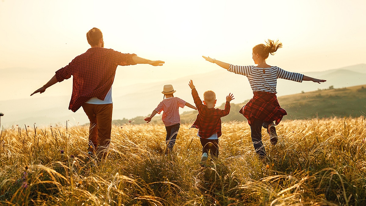 Young family running in a field, arms out, at sunset.